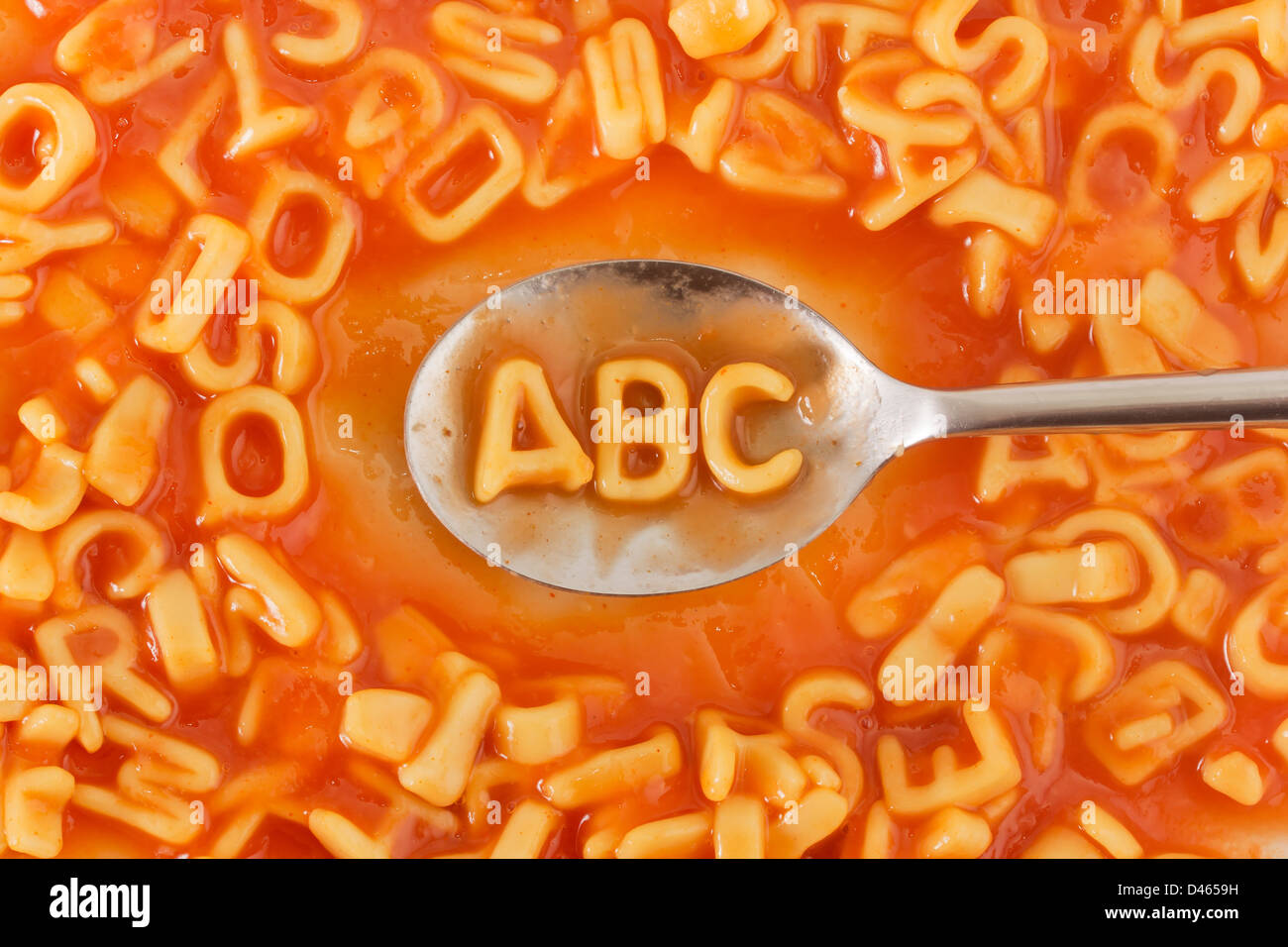 Letras ABC en forma de pasta con una cuchara dentro de cartas en forma de pasta en salsa de tomate Foto de stock