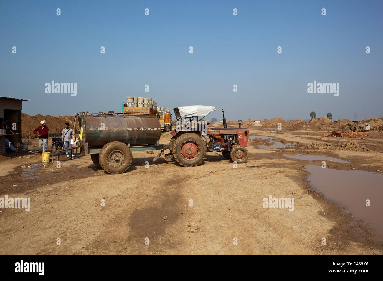 Obreros de pie cerca de un tractor y un camión cisterna en un nuevo sitio en construcción en el distrito de Mohali Chandigarh, Punjab, India Foto de stock