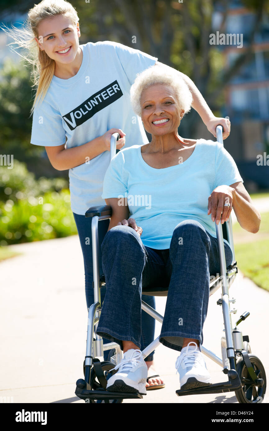 Voluntarios adolescentes empujando mujer mayor en silla de ruedas Foto de stock