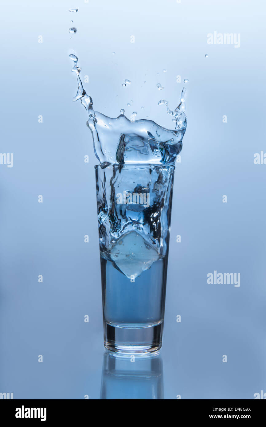 Cubo de hielo cayendo en un vaso de agua Foto de stock
