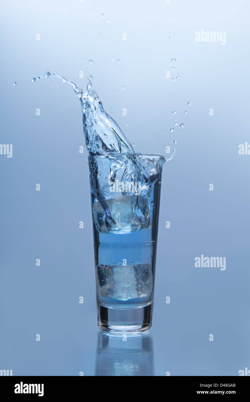 Un cubito de hielo cayendo en un vaso de agua Foto de stock