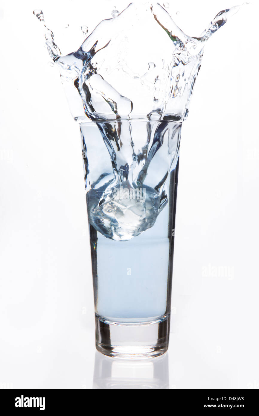 Gran cubito de hielo cayendo en un vaso lleno Foto de stock