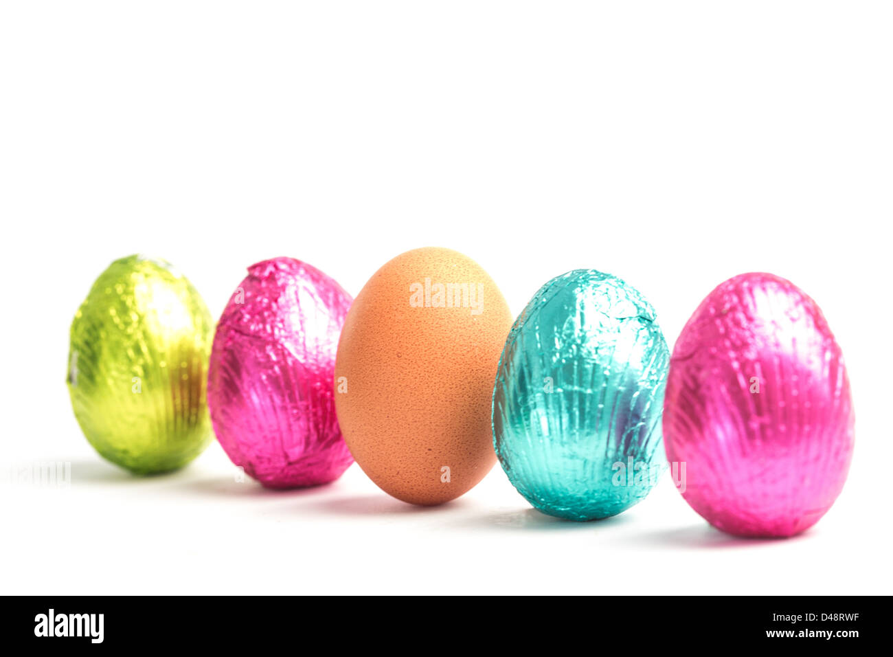Cuatro huevos de pascua en una fila con un huevo real Foto de stock