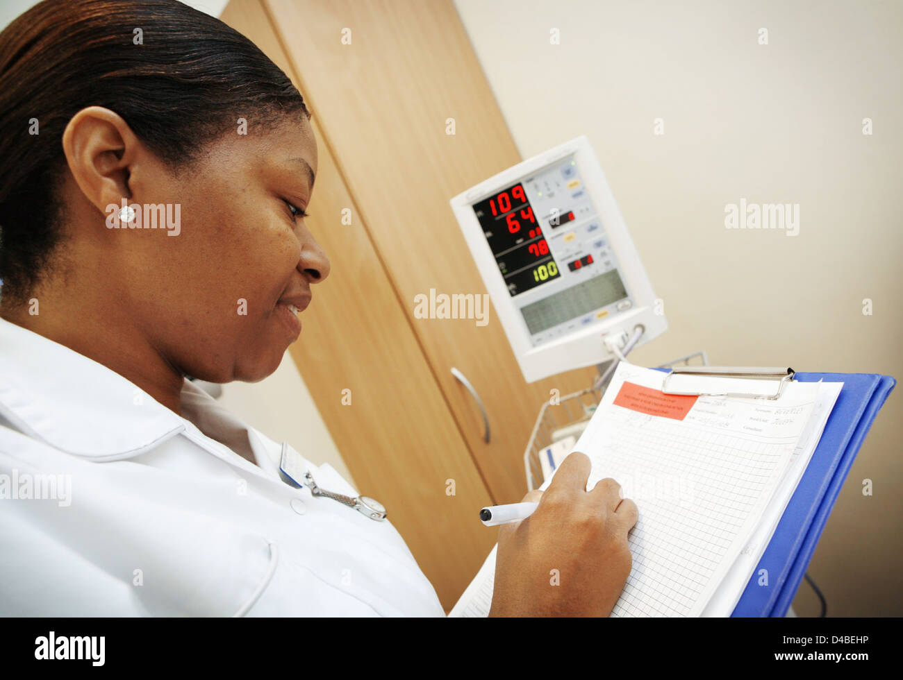 Enfermera en blanco uniforme escrito actualizaciones a sus registros de paciente Foto de stock