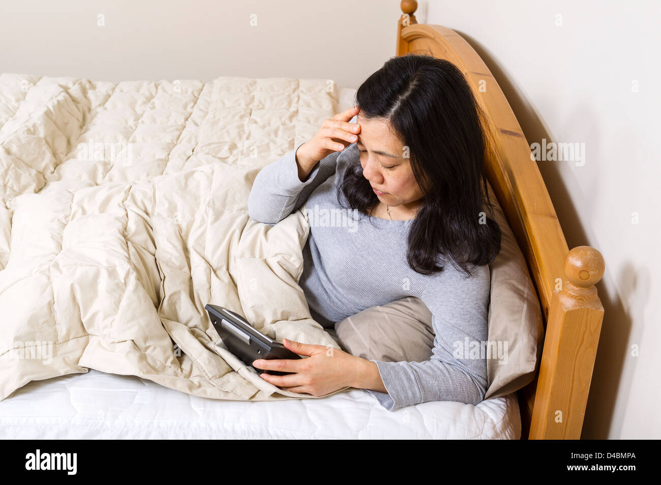 Foto horizontal de mujer madura, sentada en la cama, mientras mira el despertador en la mano Foto de stock