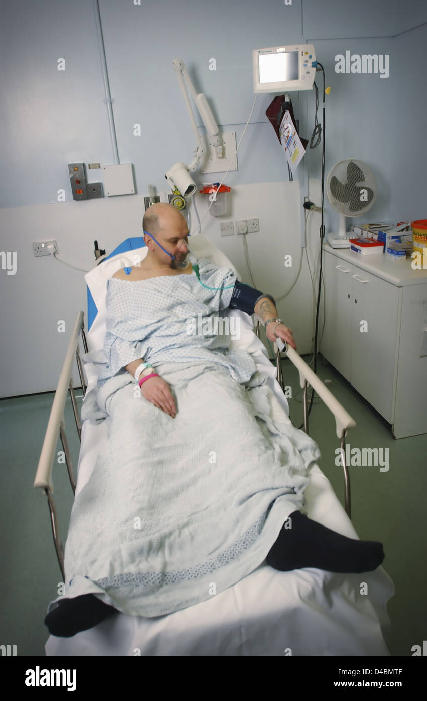 Ataque cardíaco masculino sufriente sentando en la cama con un suministro de oxígeno Foto de stock