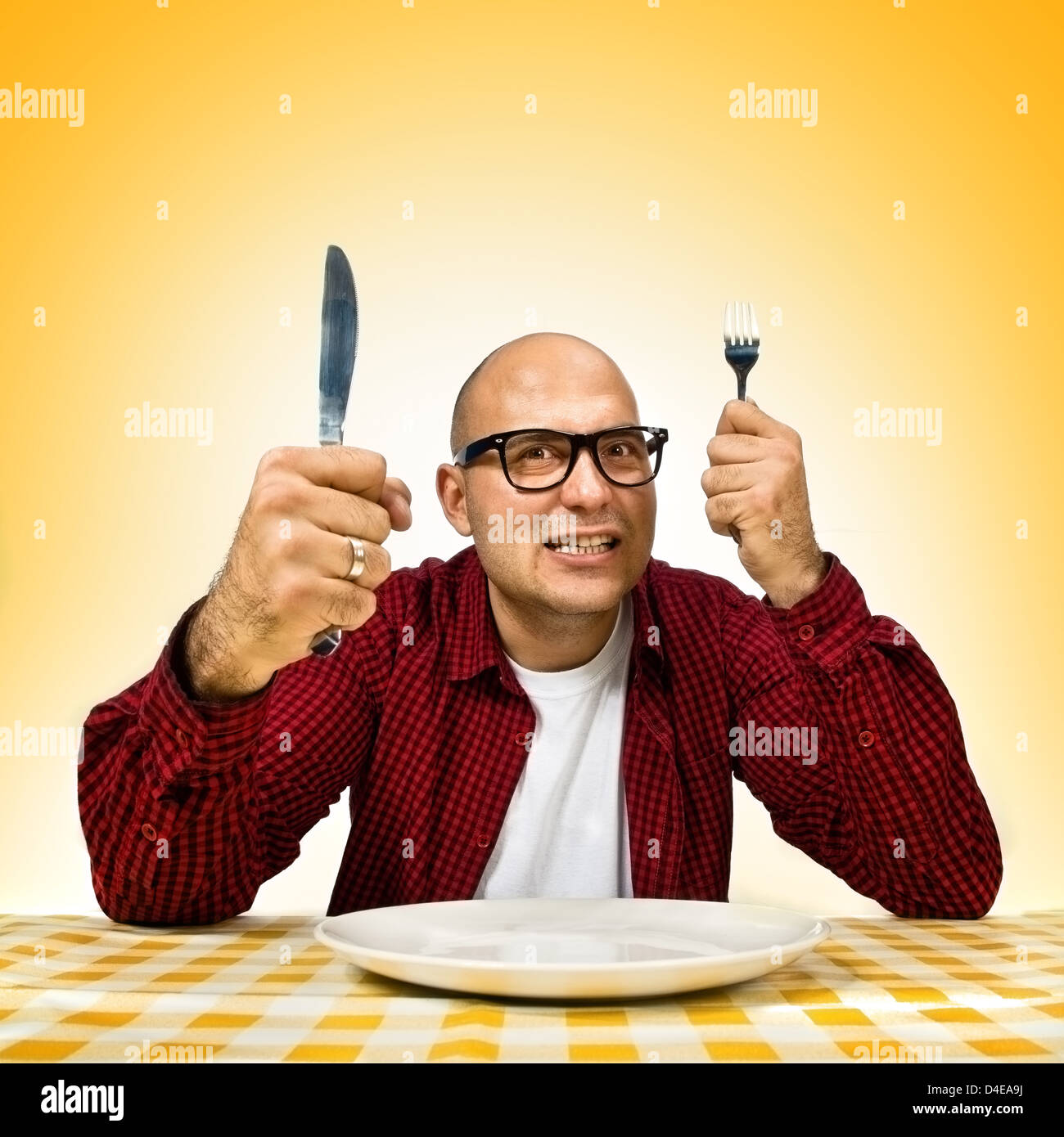 Adulto joven valiente hombre sentado en la mesa con tenedor y cuchillo planteadas. Foto de stock