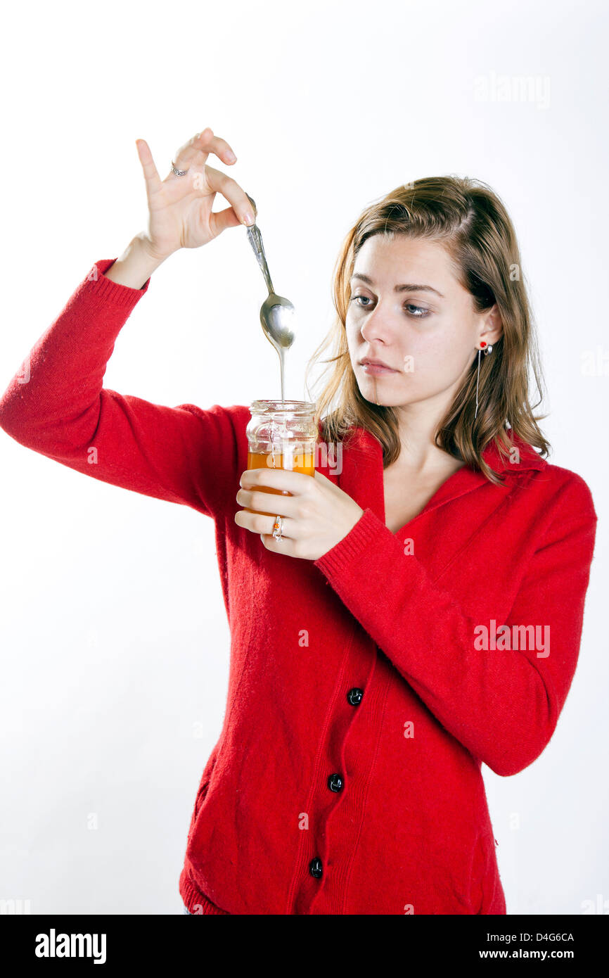 Mujer joven sosteniendo un tarro de miel y una cucharada de mirarlo Foto de stock