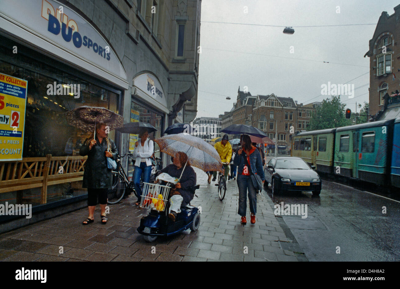 Amsterdam Holanda escena callejera en la lluvia de personas con sombrillas  mujer en scooter de movilidad Fotografía de stock - Alamy