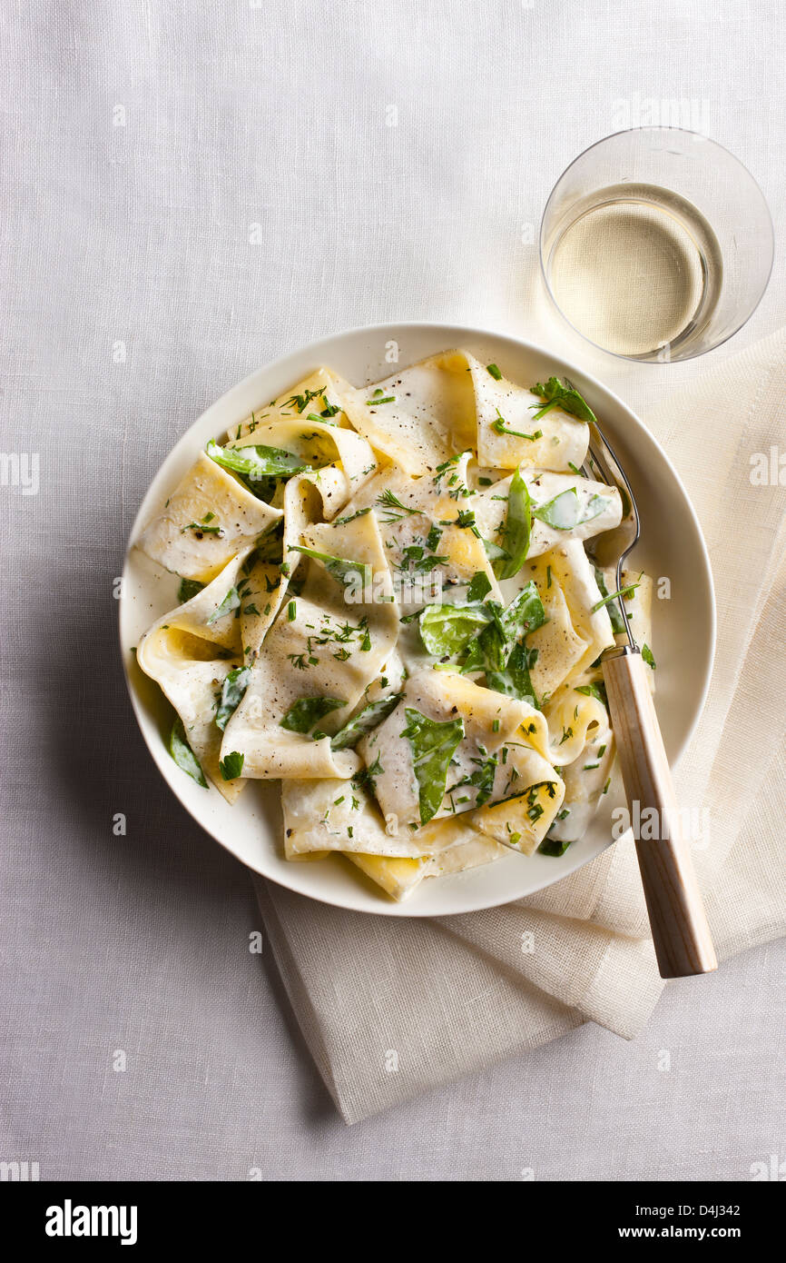Un plato de pasta pappardelle con crema de requesón, baby de espinacas frescas, hierbas y pimienta negra. Foto de stock