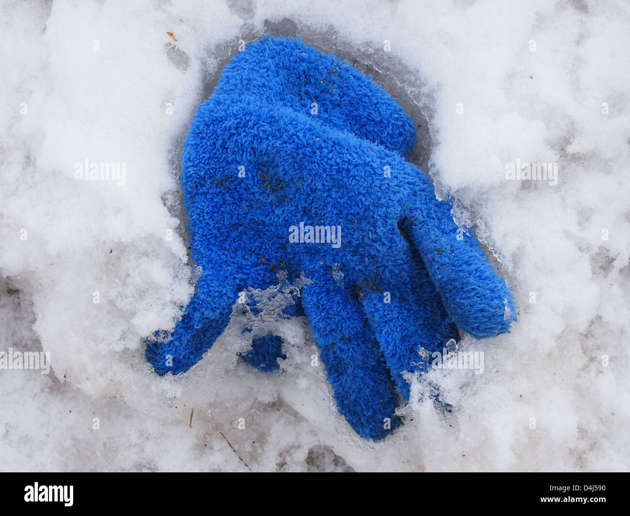 Guante azul perdido en la carretera cubierta de nieve Foto de stock