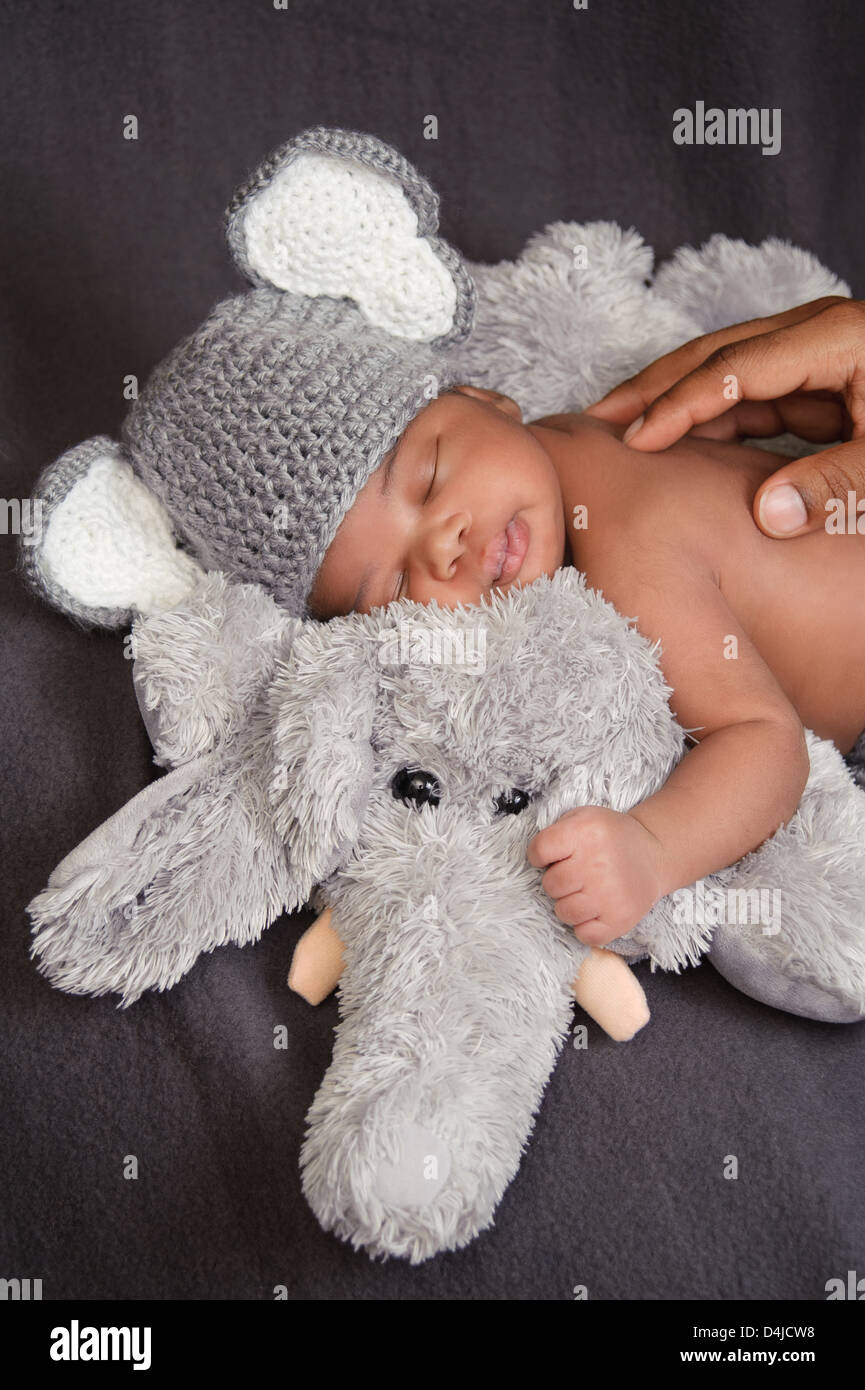 Un bebé recién nacido niño usando un sombrero de elefantes de ganchillo y dormir sobre un elefante de peluche de juguete. Foto de stock
