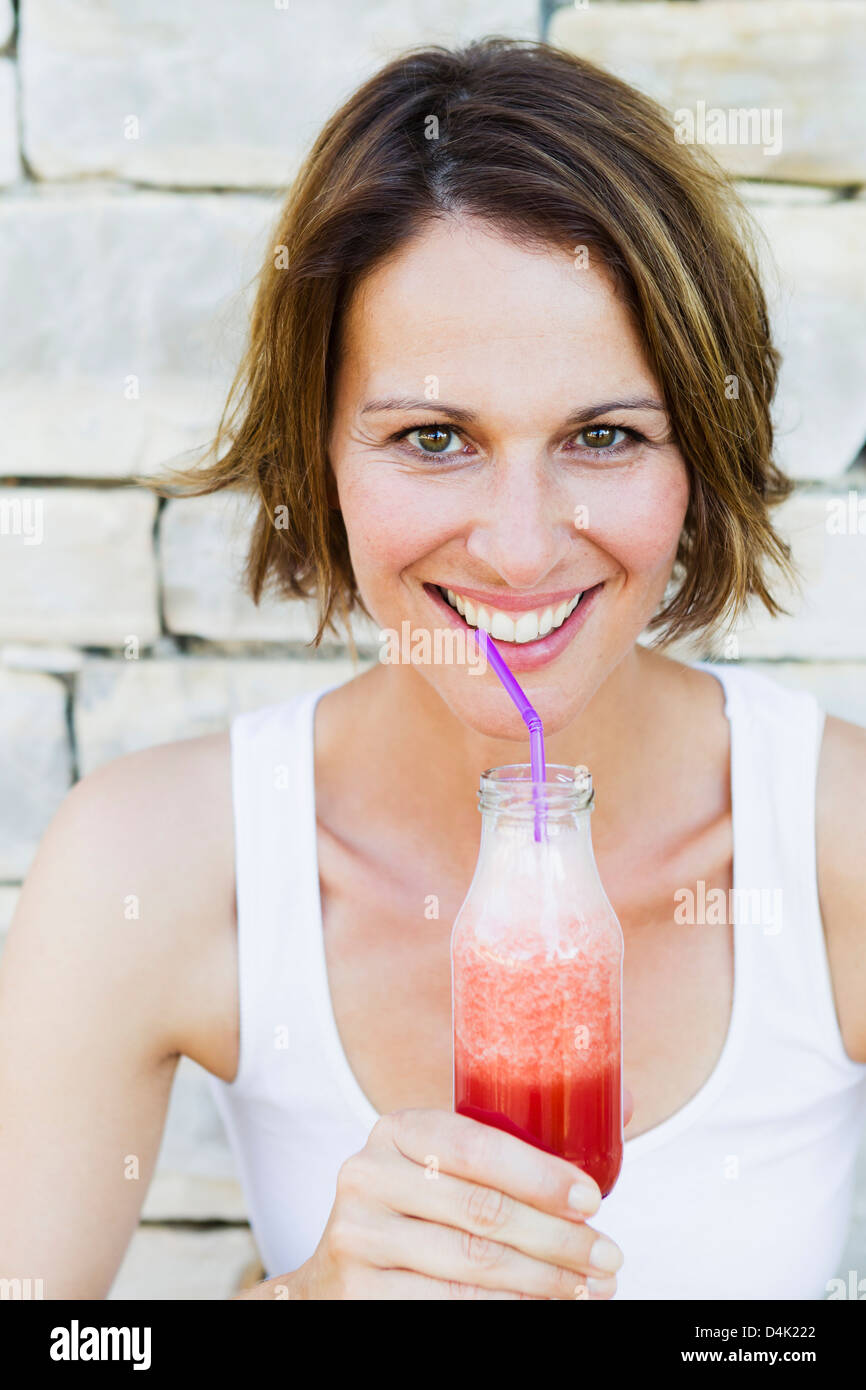 Mujer sonriente beber jugo al aire libre Foto de stock
