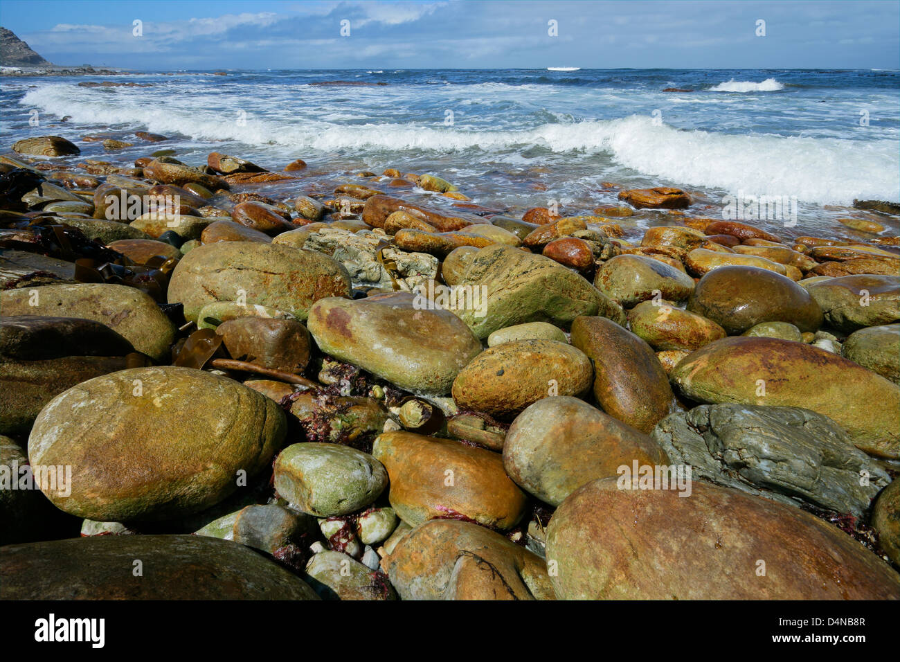 Playa rocosa con grandes cantos rodados y olas en una mañana soleada Foto de stock