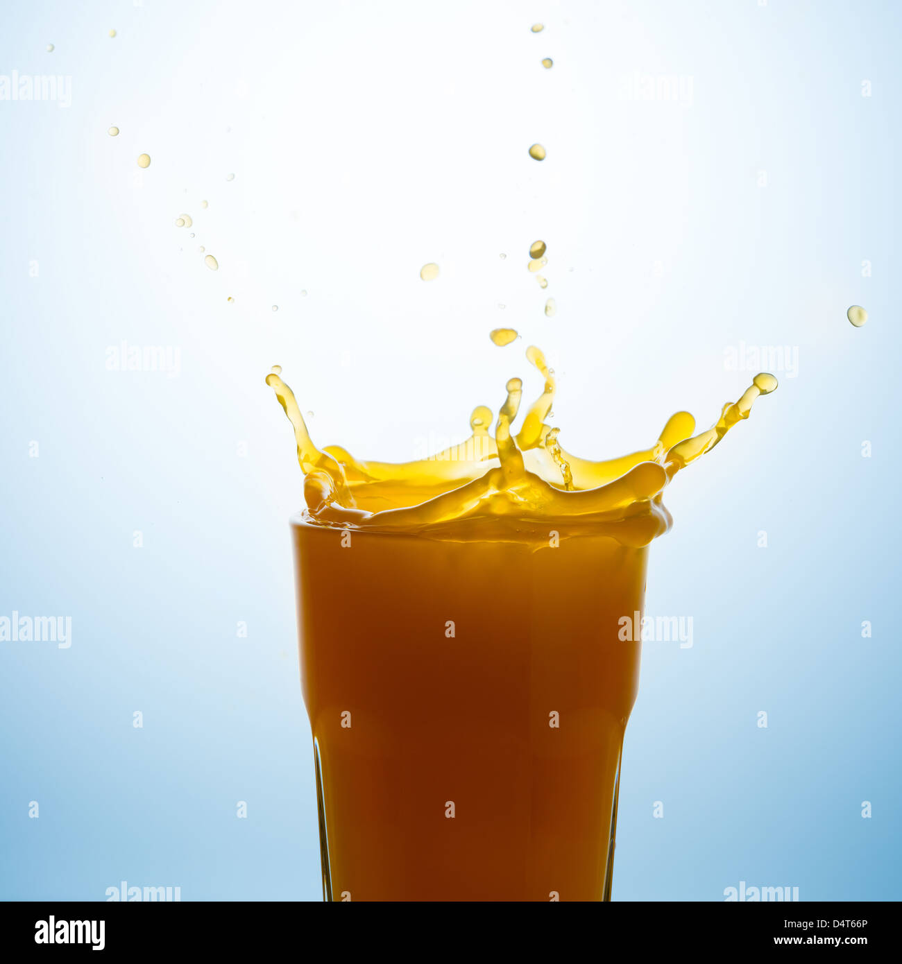 Splash en un vaso de jugo de naranja contra un fondo azul. Foto de stock