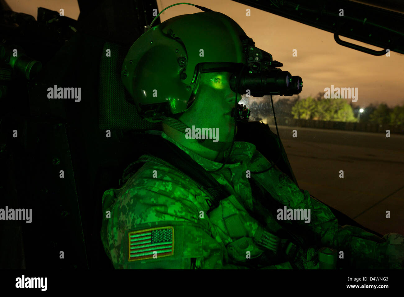 Un piloto equipado con gafas de visión nocturna en la cabina de un helicóptero Apache AH-64. Foto de stock