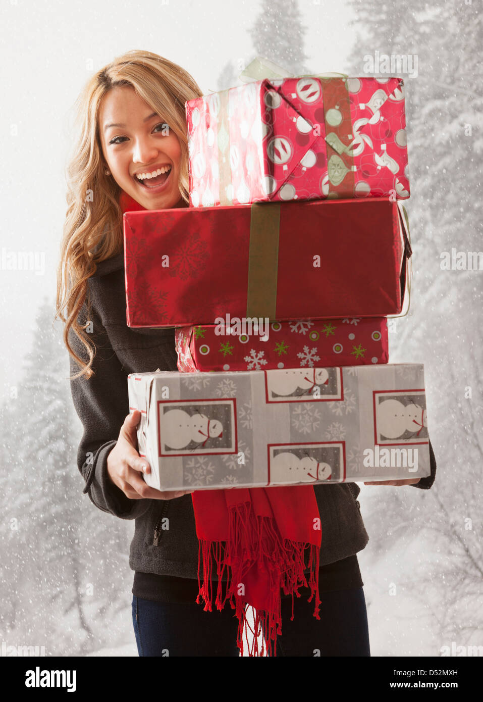Mujer de raza mixta celebración pila de regalos en la nieve Foto de stock