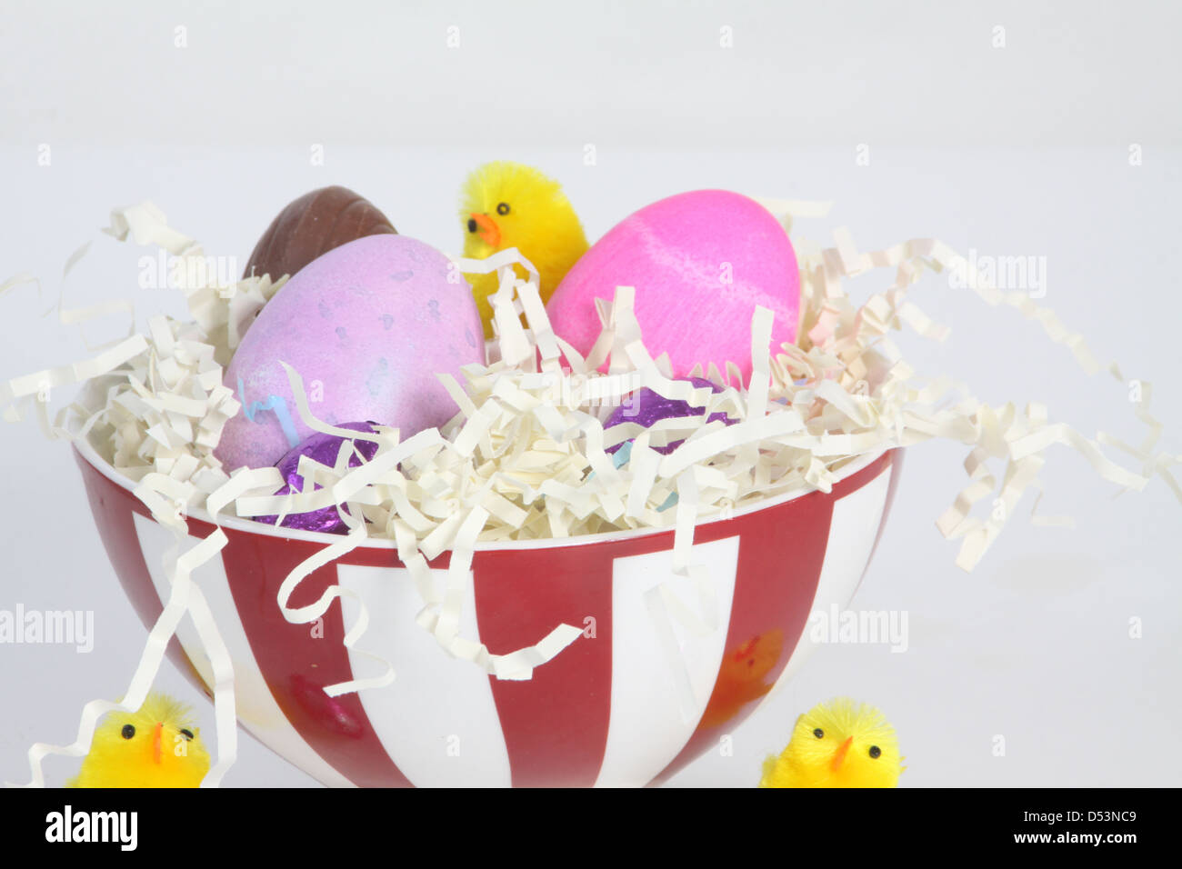 Huevos coloreados en un recipiente lleno de paja, con papel decorado para la Pascua. Foto de stock