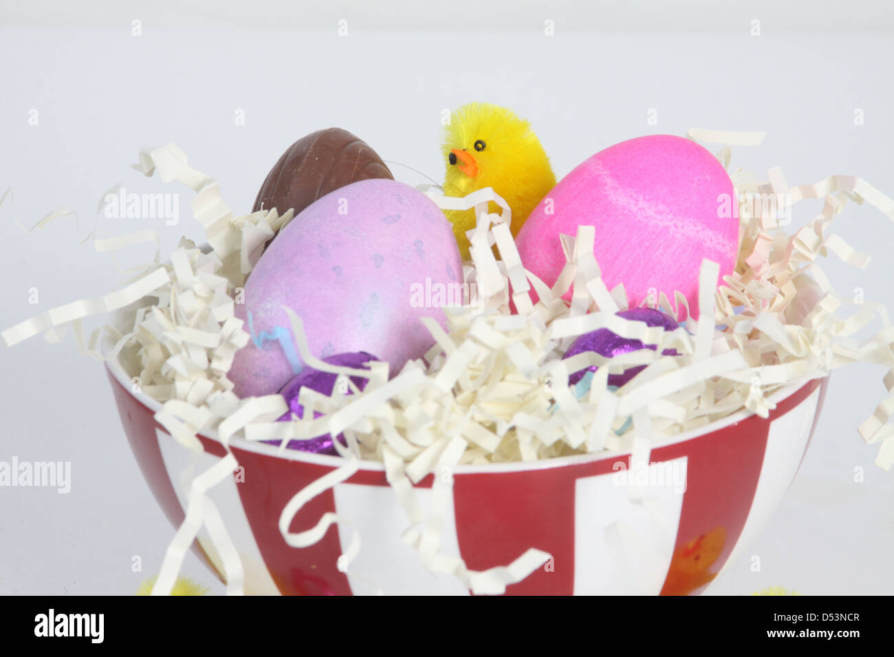 Huevos coloreados en un recipiente lleno de paja, con papel decorado para la Pascua. Foto de stock