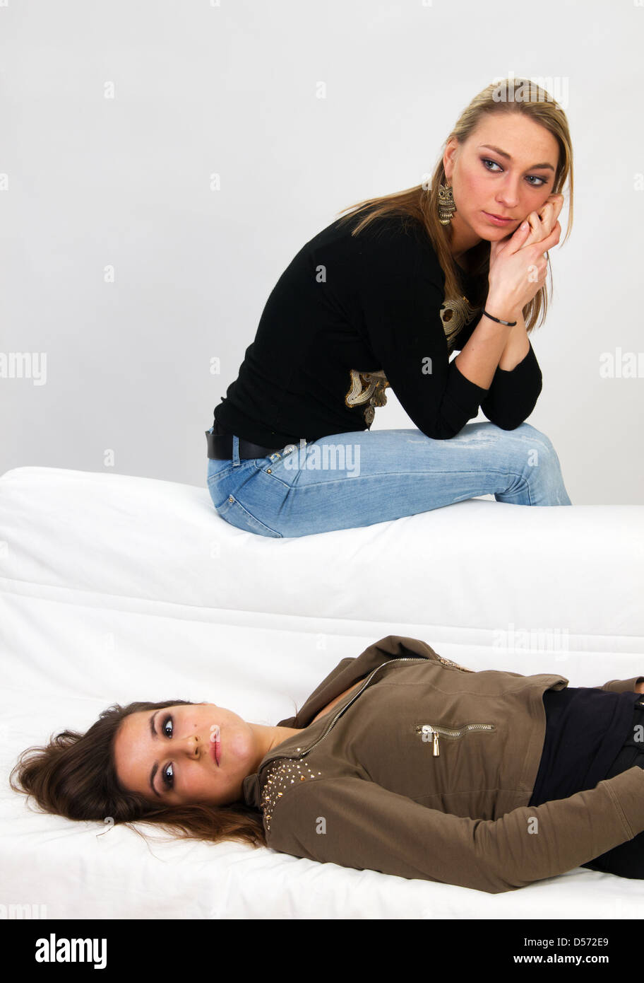 Dos jóvenes mujeres sentarse en el sofá y descontentos o aburridos o tener un argumento Foto de stock