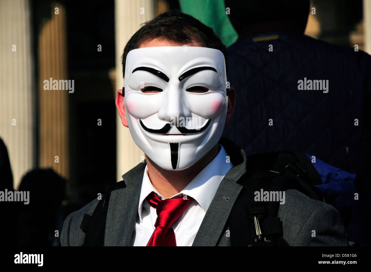 Un hombre con una corbata roja vistiendo una máscara anónima en un rally en Trafalgar Square, Londres, Reino Unido. Foto de stock