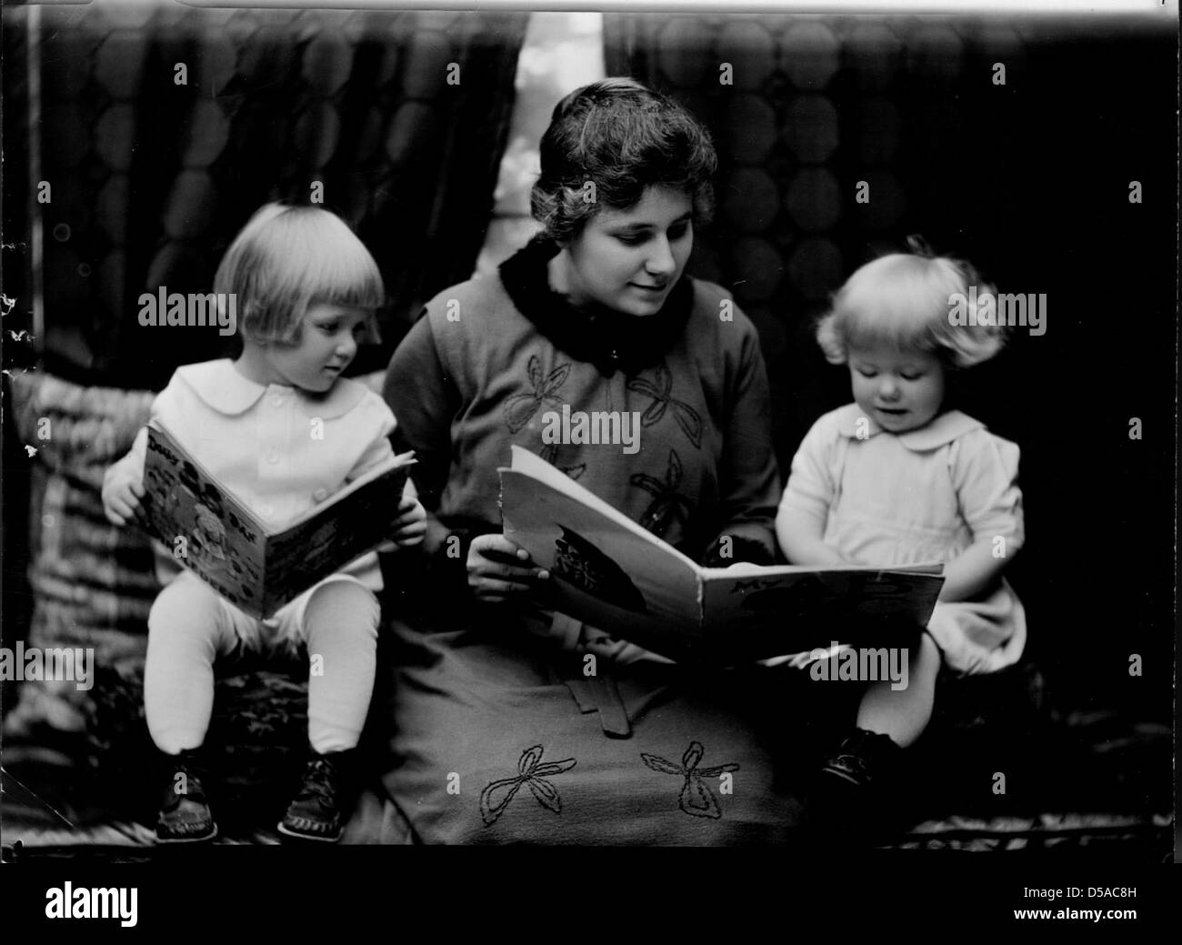 Estudiante leyendo a dos niñas pequeñas. Fotografiado en 1920 Catálogo de economía doméstica por Troy. Foto de stock