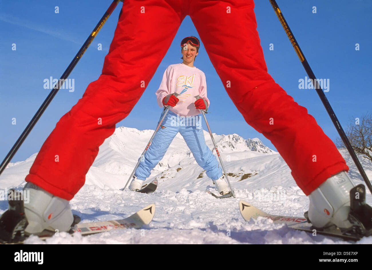 Joven esquiador vistos a través de las piernas del instructor de esquí Foto de stock