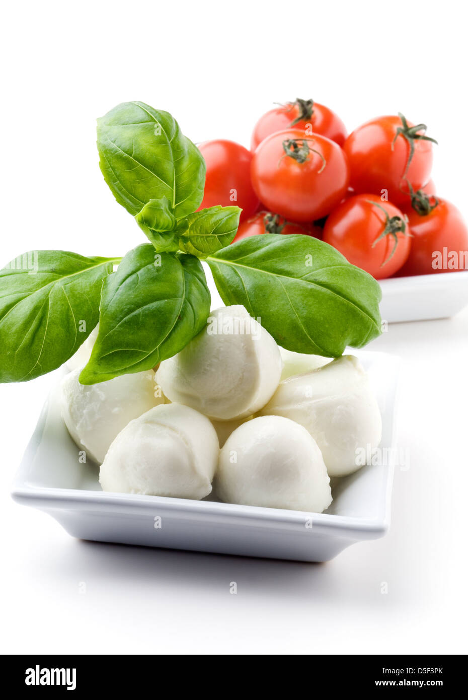 Mozzarella, tomate y hojas de albahaca fresca sobre fondo blanco. Foto de stock