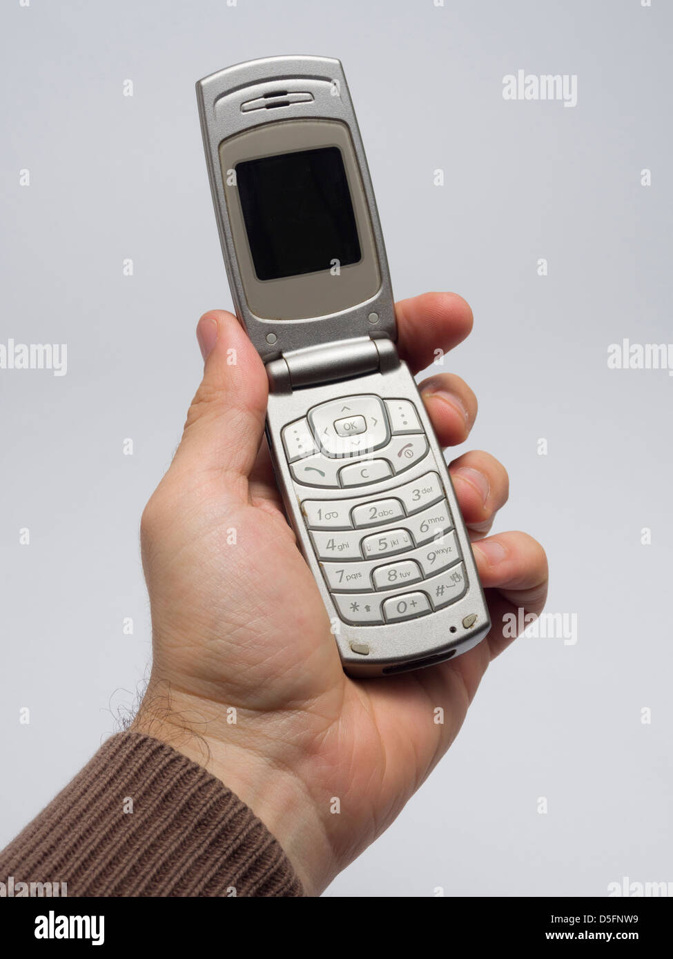 Mano sujetando antiguo teléfono móvil flip Foto de stock