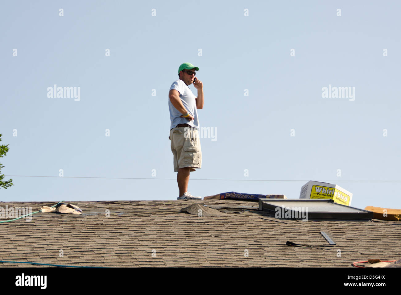 Un techado contratista está sobre un techo y conversaciones en el teléfono celular. Oklahoma, Estados Unidos. Foto de stock