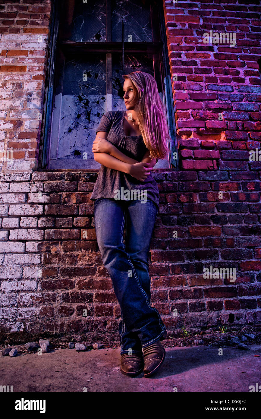 Adolescente recostada contra la pared de ladrillo con luz púrpura Foto de stock