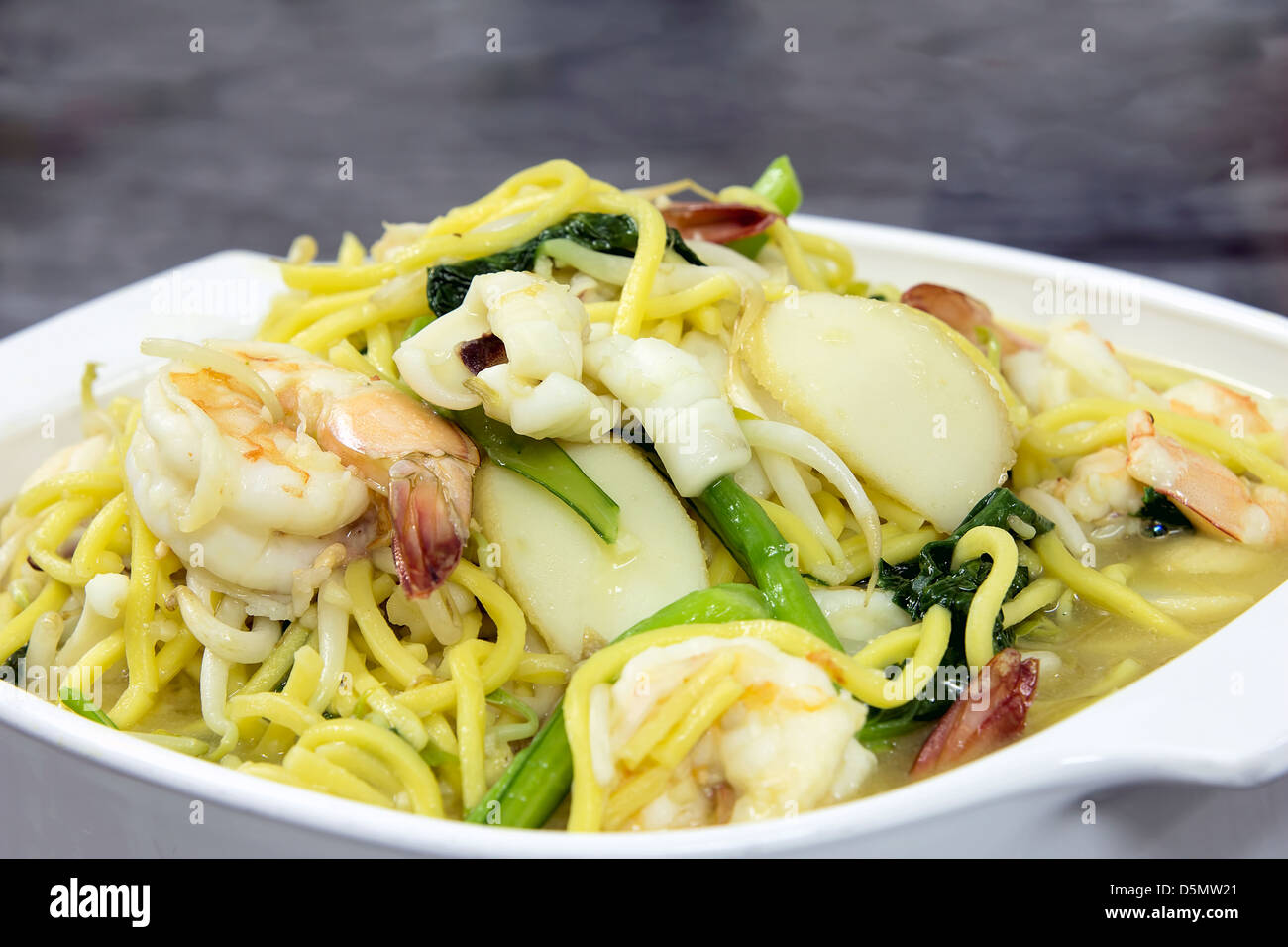 Hokkien Mee amarillo fideos salteados con gambas calamares y verduras verdes Fishcake Vista Lateral Closeup Foto de stock