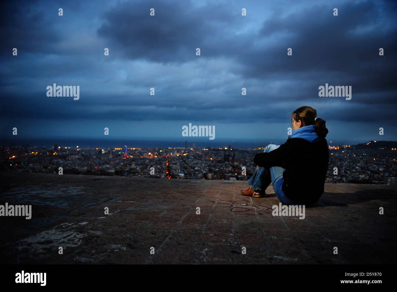 Una mujer observa el perfil de la ciudad iluminada por la noche, España. Foto de stock