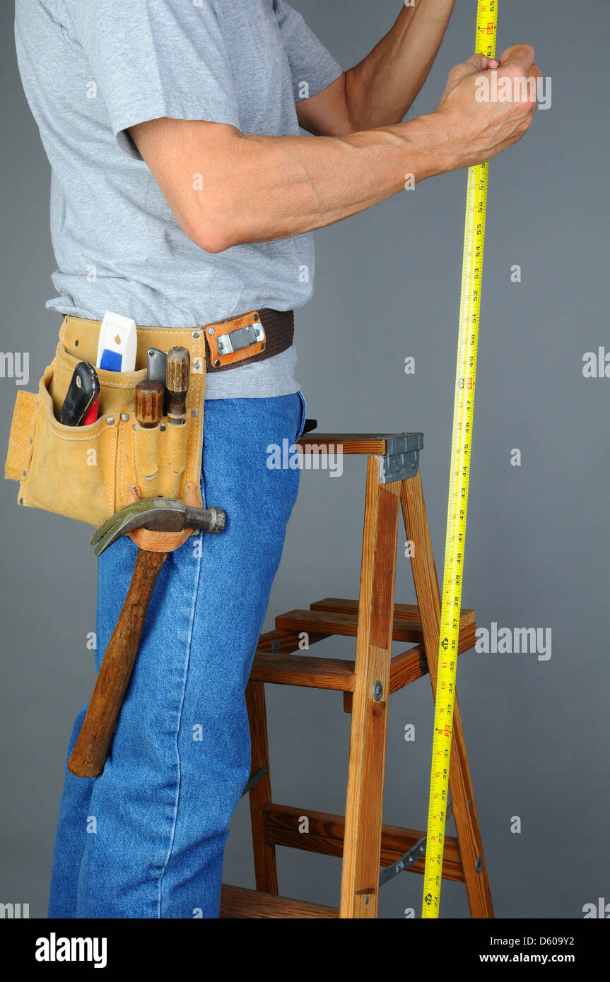 Primer plano de un contratista de pie sobre una escalera de madera sosteniendo una cinta métrica. Foto de stock