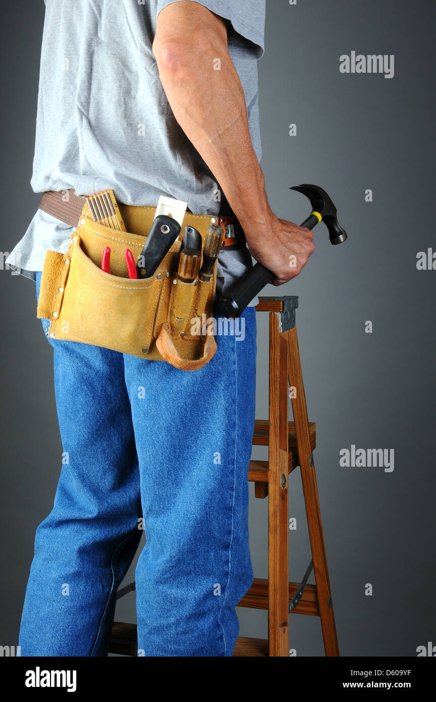 Primer plano de un contratista de pie sobre una escalera de madera sosteniendo su martillo. Formato Vertical Foto de stock