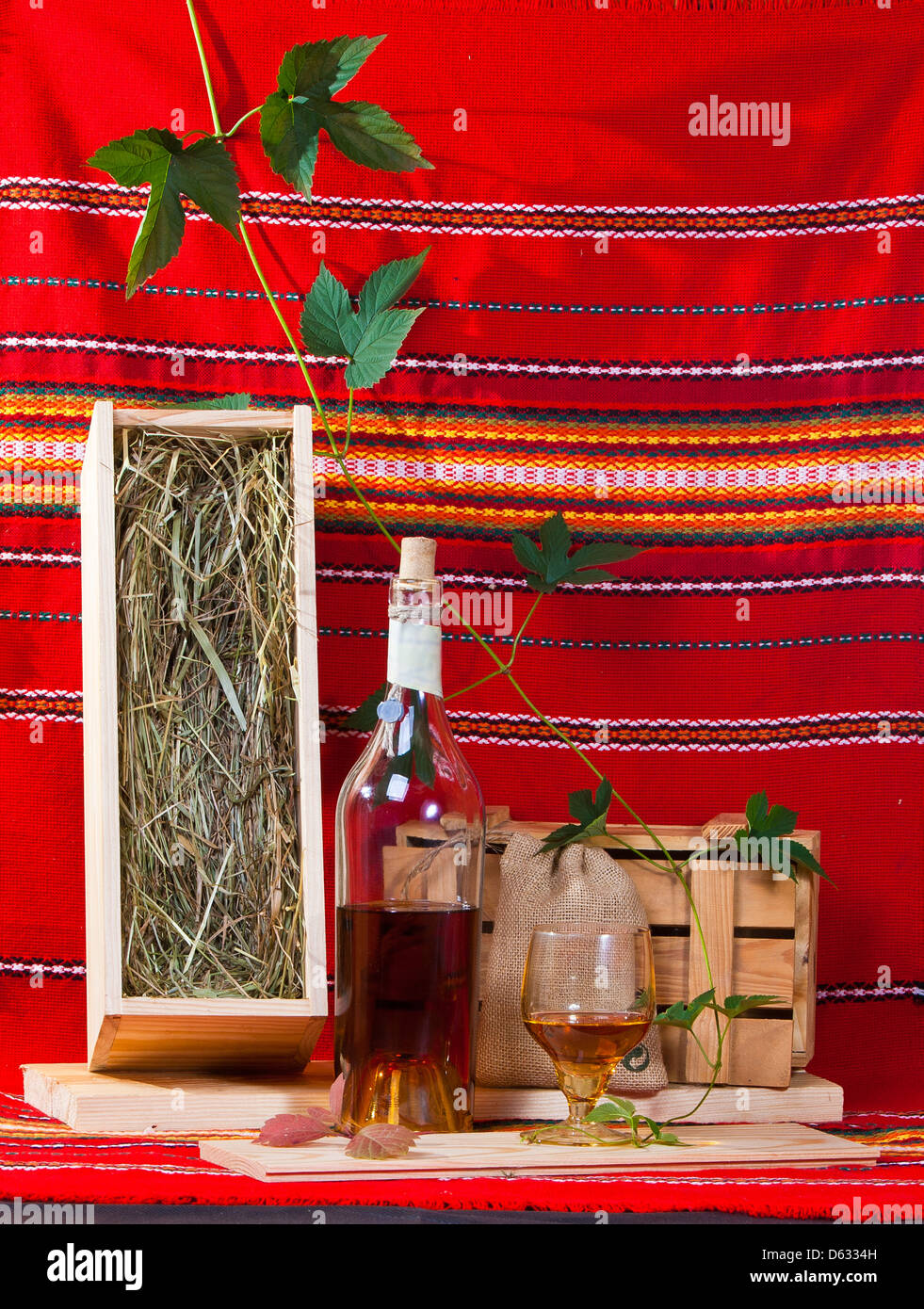 Bodegón con una botella de brandy, un cristal, cajas de madera y de vid roja sobre fondo de tela Foto de stock