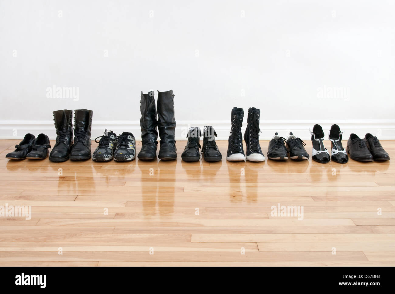 Hilera de zapatos y botas negras en un piso de madera, delante de una pared  blanca Fotografía de stock - Alamy