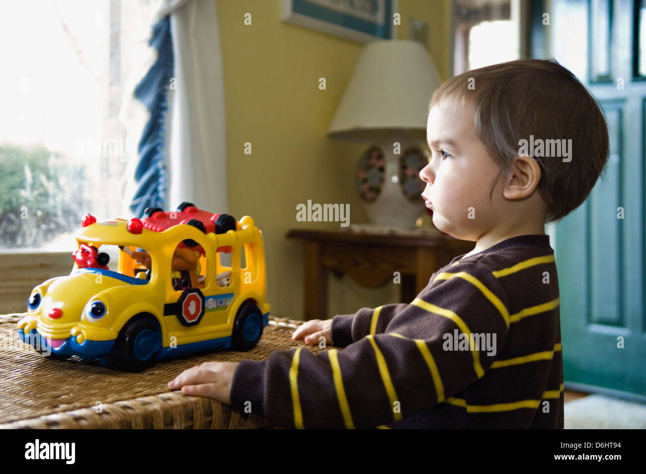 Muchacho de veintidós meses mirando por la ventana mientras jugaba con autobús escolar Toy Foto de stock