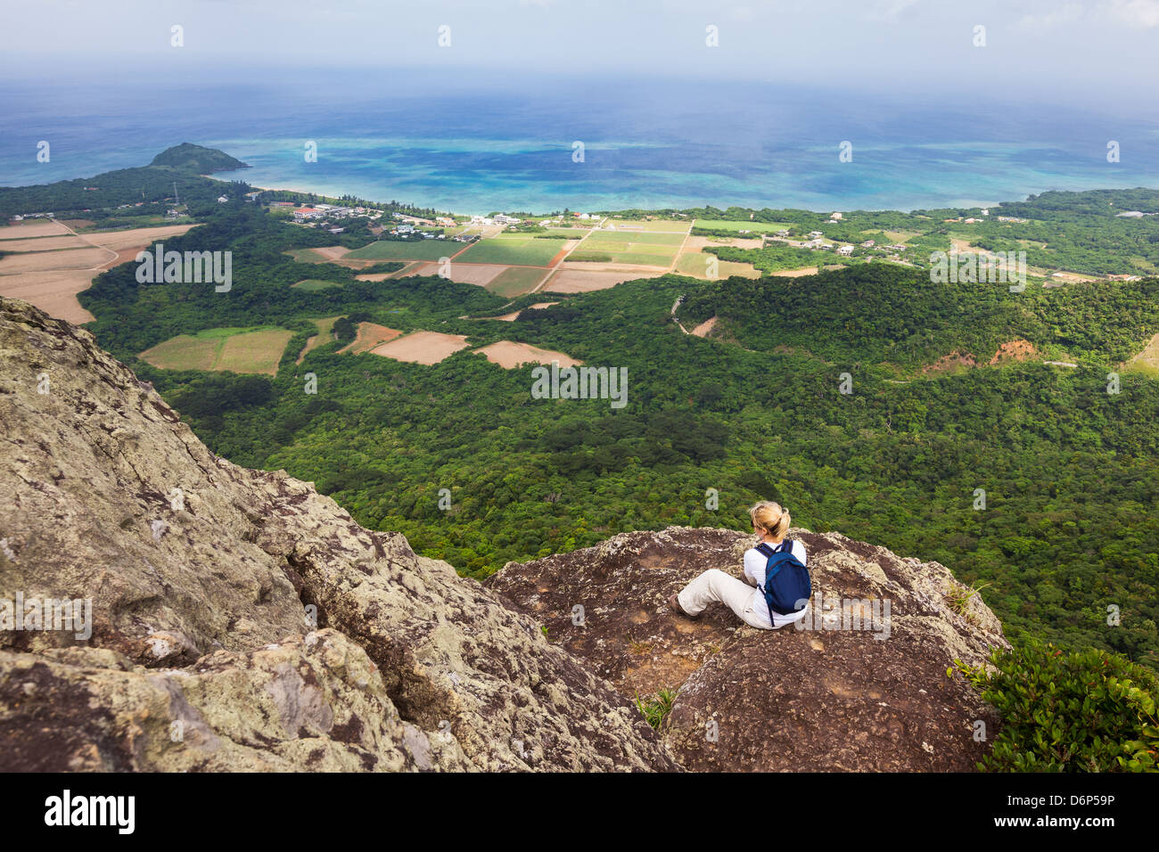 Una mujer sentada y admira la vista costera desde la cima del monte Nosoko en Ishigaki, Okinawa, Japón Foto de stock