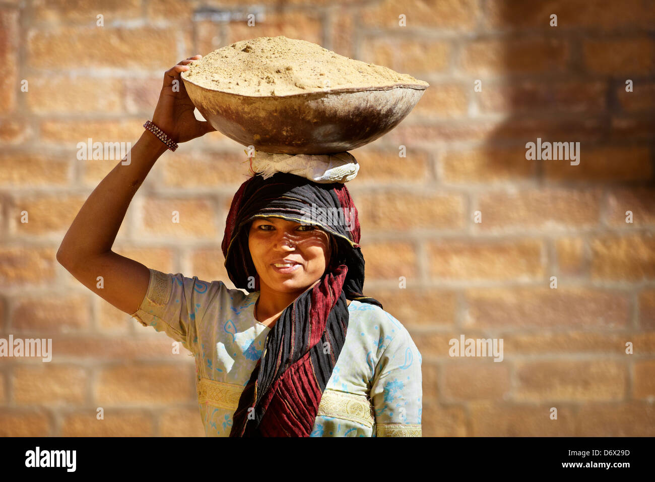 Street Scene - retrato de una mujer sonriente hindú india llevando una cesta sobre su cabeza, Jaisalmer, India Foto de stock