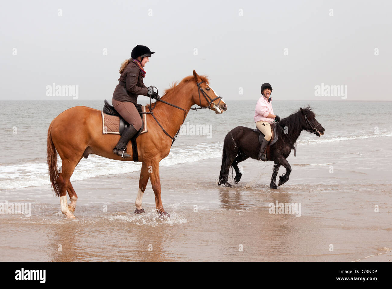 Dos mujeres jóvenes montando a caballo en Holkham Beach, al norte de la costa de Norfolk, East Anglia, en el REINO UNIDO Foto de stock