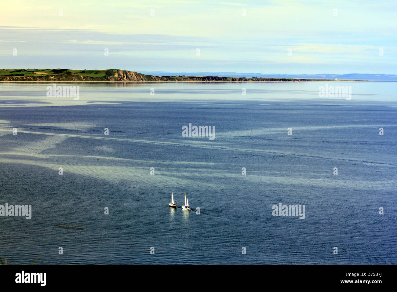 Dos veleros en una hermosa y tranquila con vistas panorámicas al mar azul junto a los acantilados de piedra arenisca en la Isla de Man Foto de stock