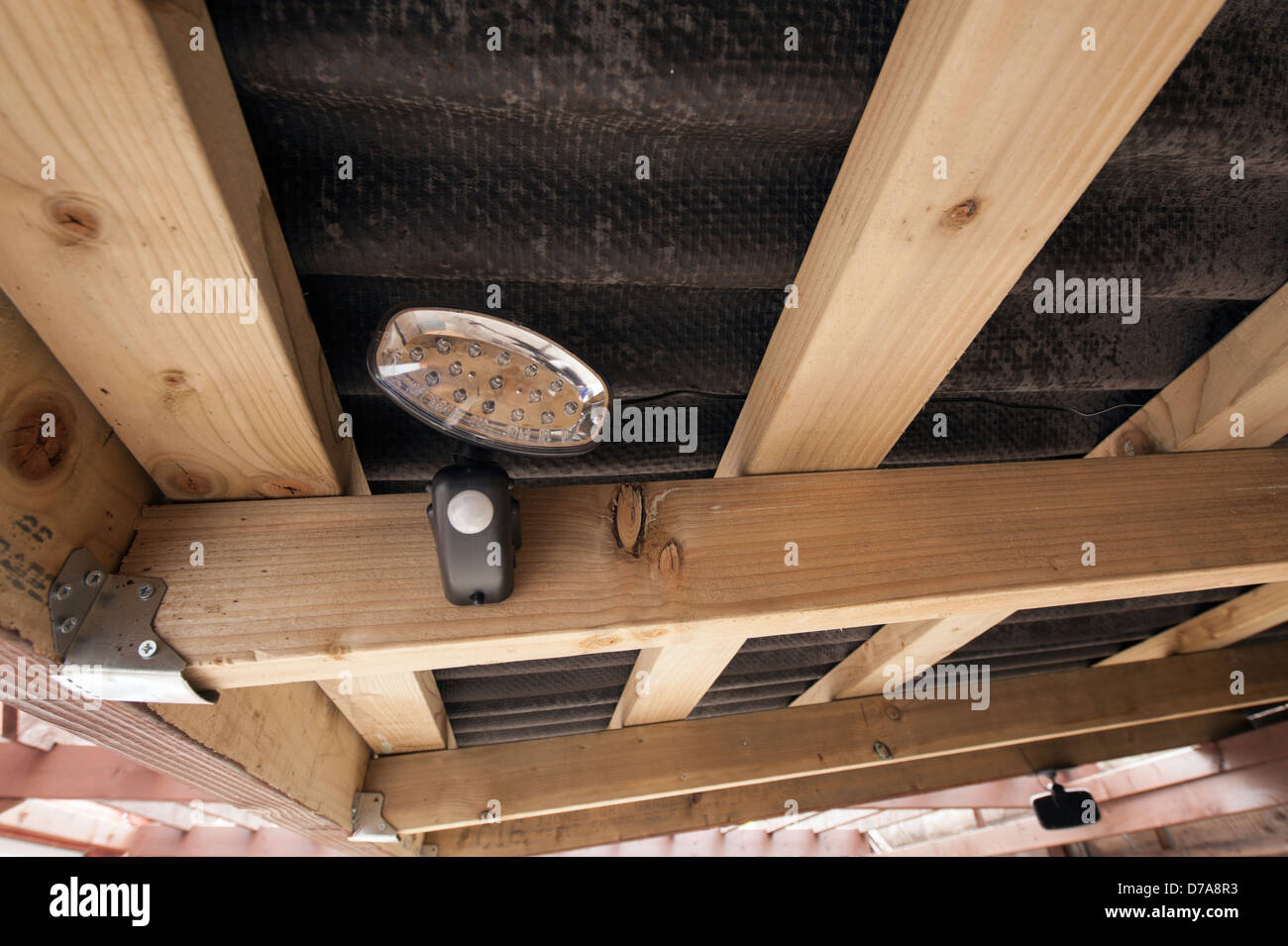 Pequeño LED luz de noche con PIR montado debajo de un betún leanedo techo con panel solar operativo cableada Foto de stock