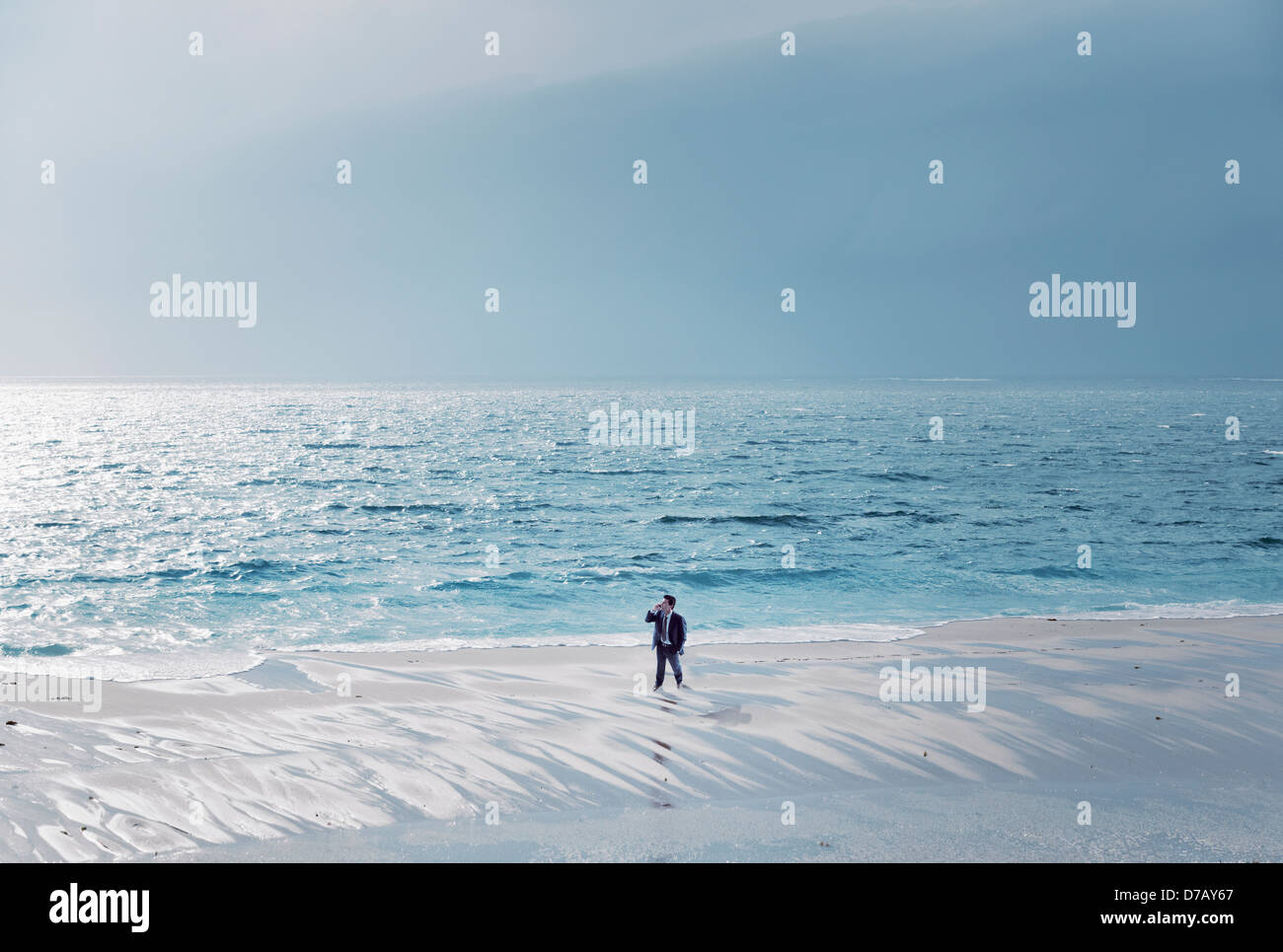 Un hombre de negocios usando un teléfono celular se sitúa en el borde del agua en la marea;Tarifa Cádiz Costa de la Luz Andalucía España Foto de stock