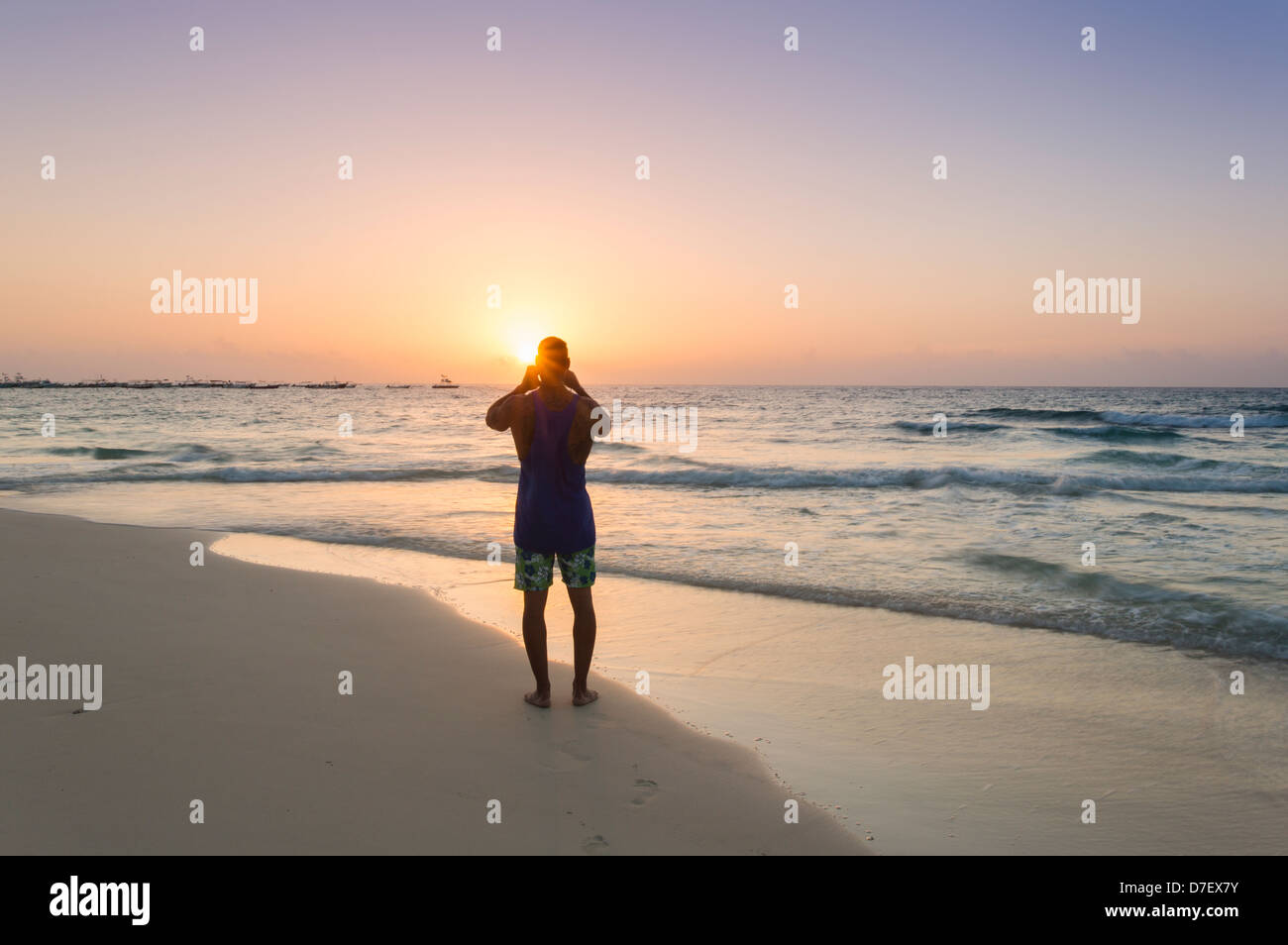 Hombre de pie en una playa en silueta fotografiando al amanecer. Foto de stock
