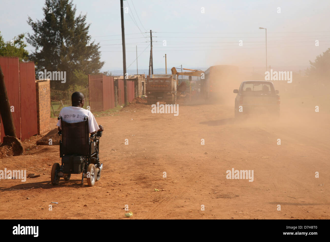 Un hombre africano luchas por una carretera de tierra en una silla de ruedas como veh Foto de stock