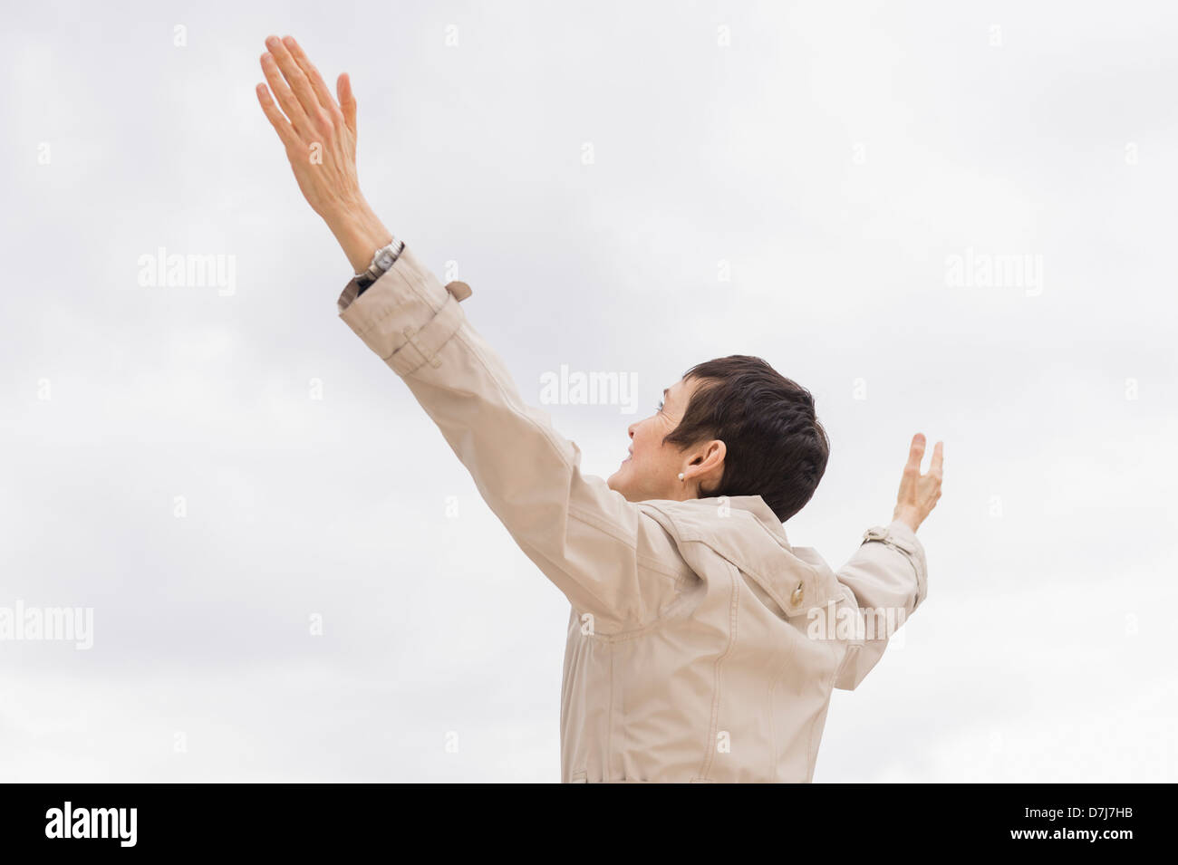 Mujer de impermeable elevando los brazos hacia el cielo nublado Foto de stock