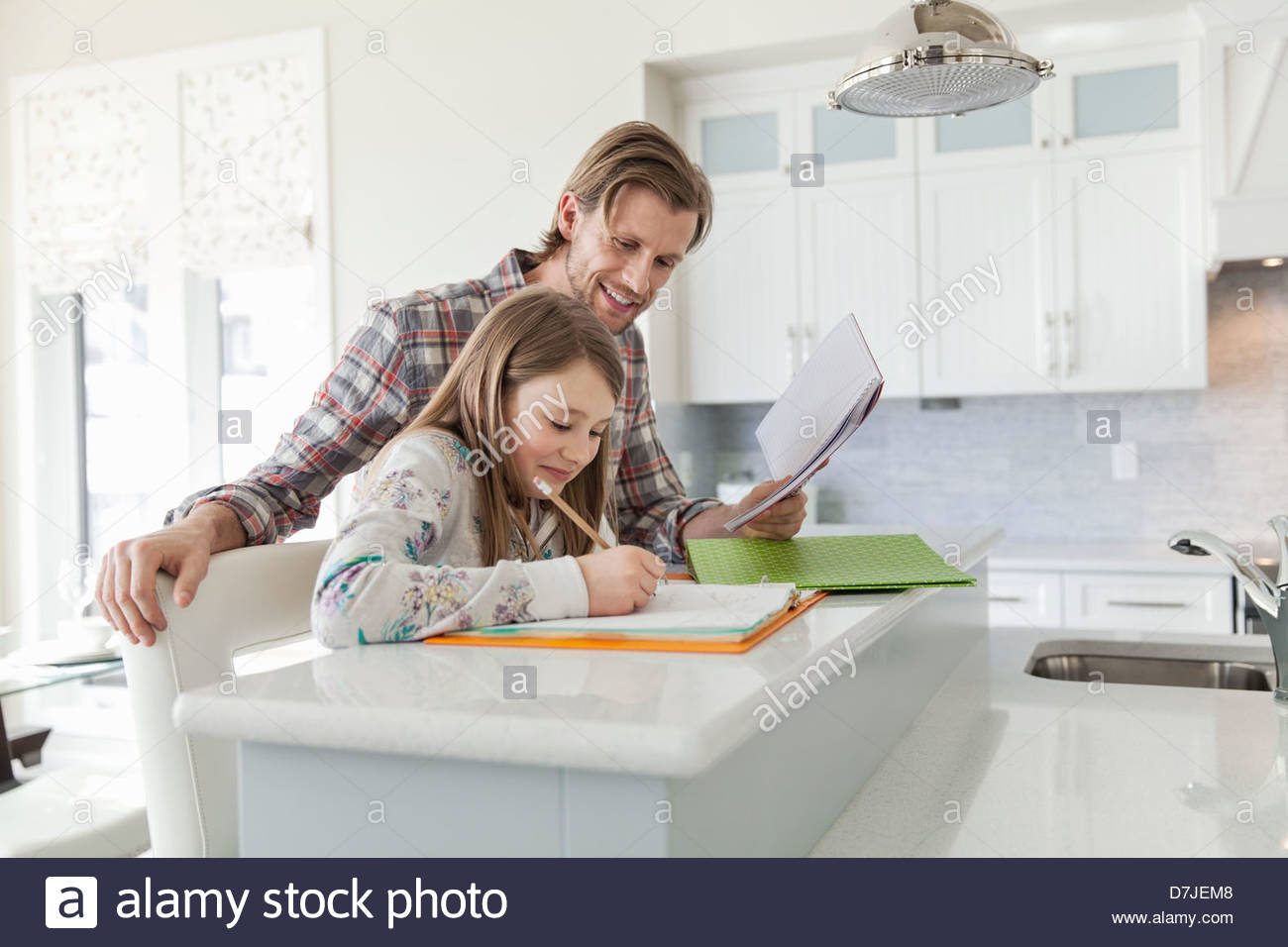Hija de padre ayudando con las tareas escolares en la isla de cocina Foto de stock
