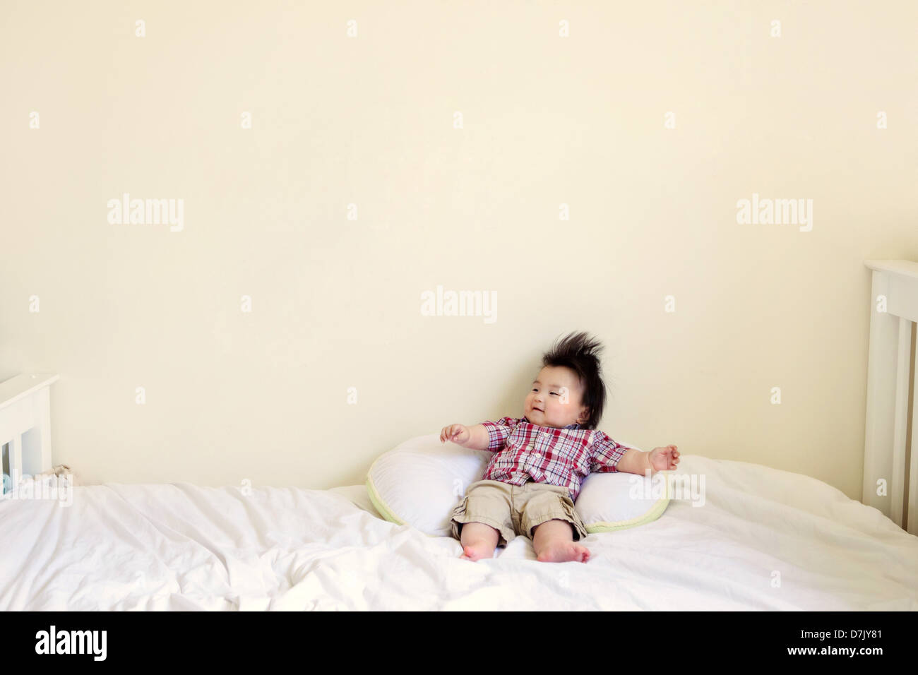 Korean American niño con cabello negro puntiagudo relajante en la cama brazos extendidos Foto de stock