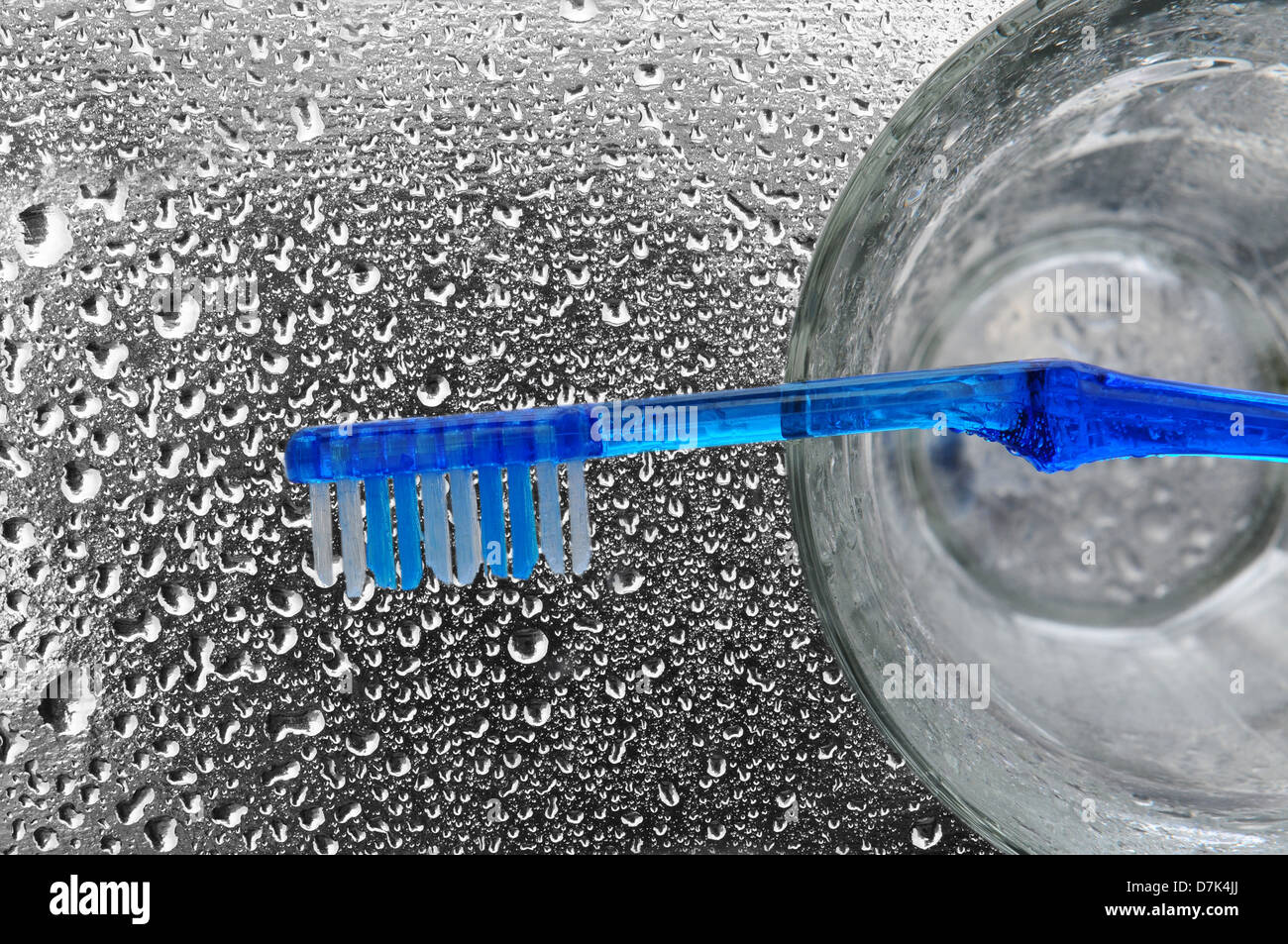 Un cepillo de dientes de color azul en la parte superior de un vaso sobre una encimera de baño mojado. Foto de stock
